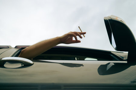 Smoking while driving, the man stretches his arm out of the car window while holding the cigaretteの写真素材