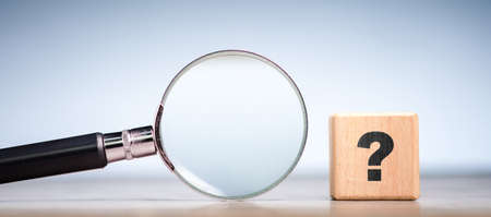 Magnifying glass with a wood cube and question mark sign, stay focus on solution, find an answer, or FAQs conceptの写真素材