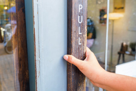 Closeup hand of a woman at the wood knob, going to pull the front door to enter the coffee shopの写真素材