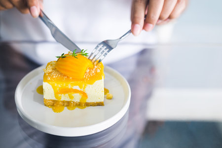 Closeup hand of a woman going to eat the Ma Yong Chid cake, Marian Plum fruit cheesecake on the glass table in the coffee shopの写真素材