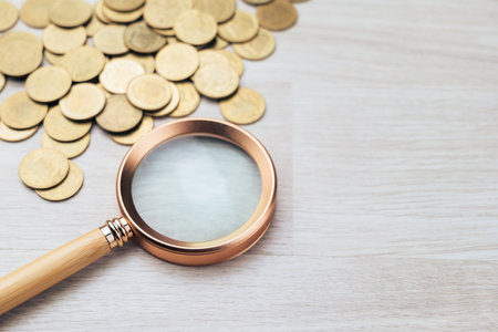 Closeup brass magnifying glass and golden money coins on the table, check the financial status, expenses, and savings, find a money sourceの写真素材