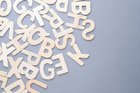 Scattered wooden white alphabets on gray background, English letters for learning English concept, glossary, words, and vocabularyの写真素材