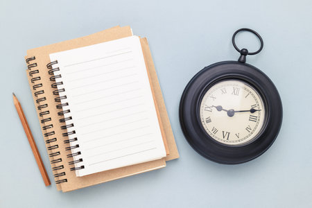 Empty white notebook on pile with a black vintage clock, writing and timing conceptの写真素材