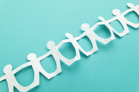 Closeup paper dolls holding hands together on green background, team, teamwork, and relationship conceptの写真素材
