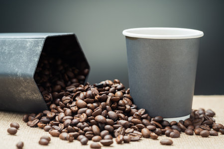 A gray paper cup with copy space placed on the pile of coffee beans that spilled out from the hexagon containerの写真素材