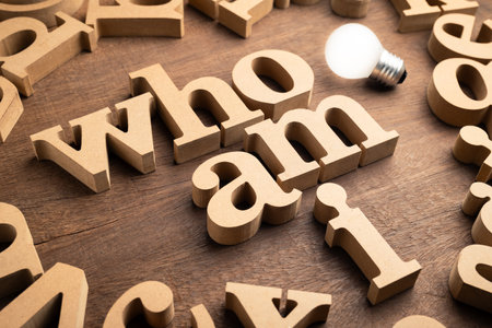 Who Am I, identity question by thick wooden alphabets with light source from a glowing bulbの写真素材