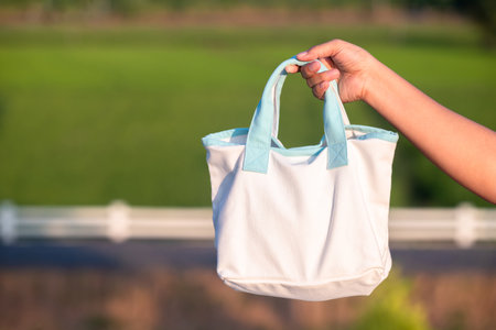 Closeup a woman carrying a white handbag made of cloth on a green environment backgroundの写真素材
