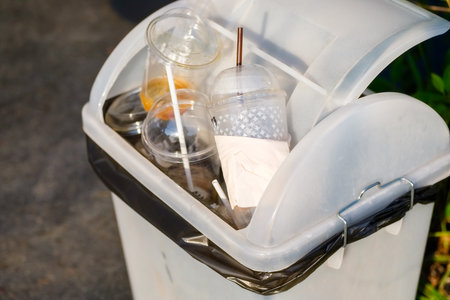 Many plastic cups are left at the top of the public trash bin, waste single-use cold drinks with strawsの写真素材