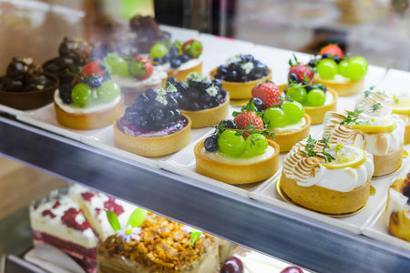 Closeup fruit cake topped with grape, strawberry and blueberry, with other decorated cakes in the...