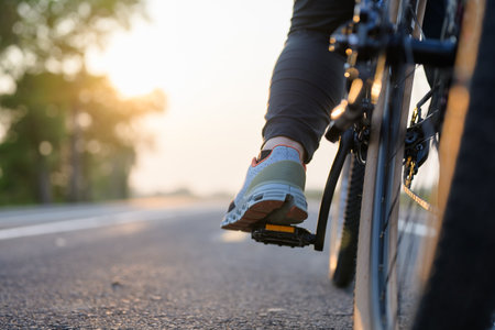 Closeup foot of the bicycle rider on the pedal while riding along the asphalt road in countryside at sunsetの写真素材