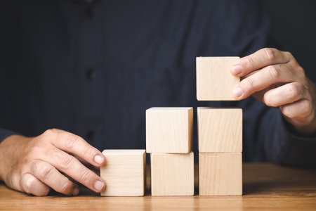 Man playing wooden cubes, arrange it as step stairs on the table, business plan concept, improvement, career progress, build a successの写真素材