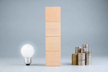 Light bulb and heap of coins, with stack of wood cubes as the wall between it, the money that is on the other side of the crative idea, making money conceptの写真素材