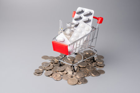 Many medicines in a mini shopping cart placed on the pile of coins, buying medicines, drugs costsの写真素材