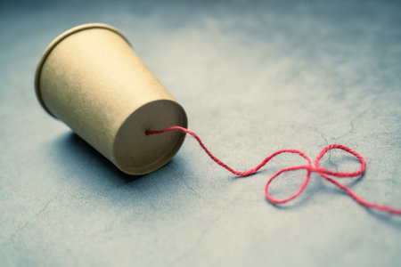 A brown cup with red string as the other end of a line of an old style cup phone, communication...