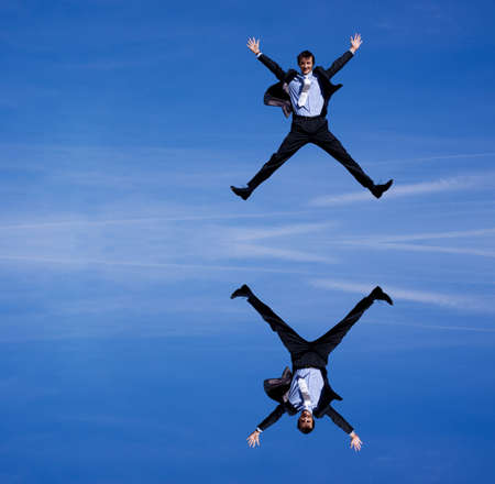 Reflection of a businessman jumping against blue skiesの写真素材