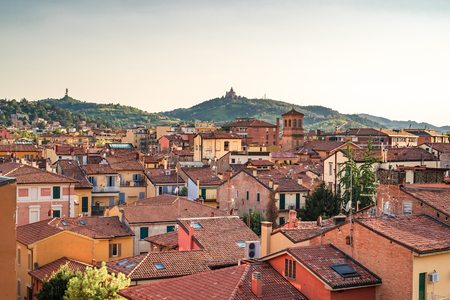 Bologna, Emilia Romagna, Italy. The roofs of city at sunset: Basilica of San Luca on the background.の写真素材
