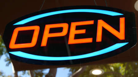 Open neon sign glowing in the dark. Vivid retro styled text at entrance on glass window. Colorful...