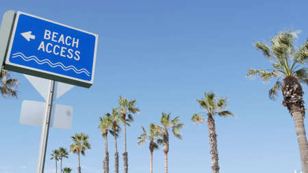 Beach sign and palms in sunny California, USA. Palm trees and seaside signpost. Oceanside pacific tourist resort aesthetic. Symbol of travel holidays and summertime vacations. Beachfront promenade.の写真素材