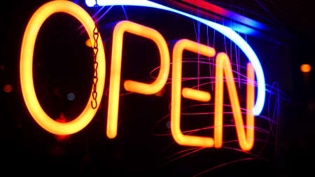 Open neon sign glowing in the dark. Vivid retro styled text at entrance on glass window. Colorful electric banner selective focus close up. Light bulbs radiance at night. Shiny illuminated lettering.の写真素材