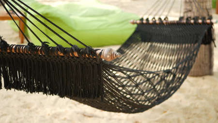 Black hammock stretching between coconut palms. Mesh vintage hipster hammock with fringe on edges stretched on sandy paradise beach of tropical island. Relax, travel vacation holiday resort conceptの写真素材