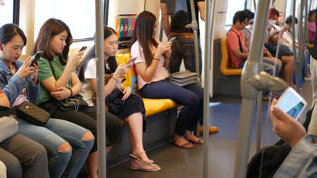 BANGKOK, THAILAND - JULY 13, 2019: Asian passengers in train using smartphones. Thai people online...