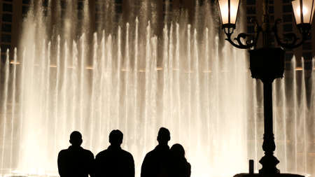 LAS VEGAS, NEVADA USA - DEC 13, 2019: People looking at Bellagio fountain musical performance at night. Contrast silhouettes and glowing dancing splashing water. Entertainment show in gambling city.のeditorial素材