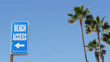 Beach sign and palms in sunny California, USA. Palm trees and seaside signpost. Oceanside pacific tourist resort aesthetic. Symbol of travel holidays and summertime vacations. Beachfront promenade.の写真素材