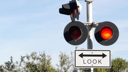 Level crossing warning signal in USA. Crossbuck notice and red traffic light on rail road intersection in California. Railway transportation safety symbol. Caution sign about hazard and train track.の写真素材