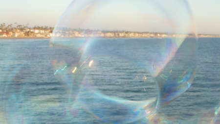 Blowing soap bubbles on ocean pier in California, blurred summertime background. Creative romantic...