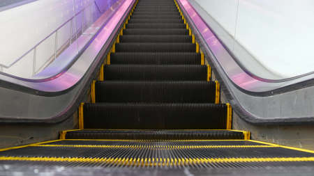 Low angle looped perspective view of modern escalator stairs. Automated elevator mechanism. Yellow...