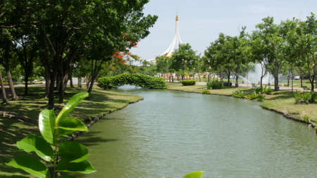 BANGKOK, THAILAND - 12 JULY, 2019: Blooming garden near pavilion in park. Green trees and flowers growing near pavilion building against cloudless blue sky on sunny day in King Rama IX Parkのeditorial素材