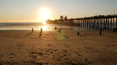 Oceanside, California USA - 27 Dec. 2019: Wooden pier and people walking. Tourists strolling in waterfront resort, summertime vacations near Los Angeles. Sunset ocean beach, tropical sunny orange sky.のeditorial素材