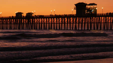 Oceanside, California USA - 16 Feb 2020: Surfer silhouette, pacific ocean beach in evening, water waves and sunset. Tropical coastline, waterfront vacation resort. People enjoy surfing as sport hobby.のeditorial素材