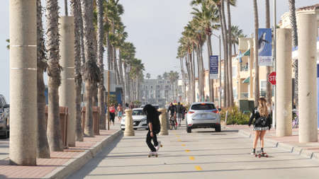 Oceanside, California USA - 8 Feb 2020: People on waterfront promenade, beachfront boardwalk near pier. Vacations ocean beach resort near Los Angeles. Man and woman skateboarding, teens on skates.のeditorial素材