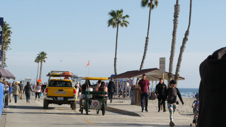 Oceanside, California USA -16 Feb 2020: People walking strolling, waterfront sea promenade, beachfront boardwalk near pier. Vacations ocean beach resort near Los Angeles. Lifeguard car, surrey bike.のeditorial素材