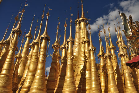Exterior of exotic temple with stupas and payas, From below shot of golden bright stupas of temple on lake Inle under blue sky, Myanmar. Sacred place.の写真素材