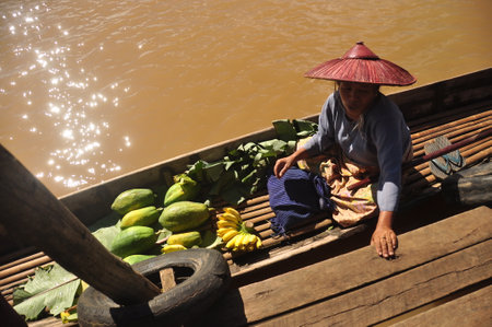 INLE, MYANMAR - NOVEMBER 29, 2015: Ethnic woman on boat with green vegetables, From above of ethnic senior woman on boat near local market with green fruit.のeditorial素材