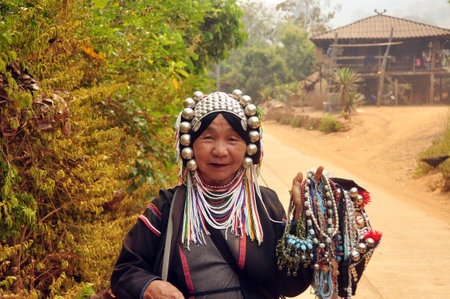 CHIANG MAI, THAILAND - MARCH 1, 2013: Mature ethnic woman with traditional attire in authentic gown and headwear holding heap of traditional adornments in village. Noth tribes Akha, Lisu, Karen, Lahuのeditorial素材
