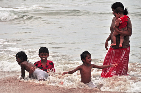HIKKADUWA, SRI LANKA - 18 DECEMBER 2011 View of adult ethnic woman with group of kids splashing in ocean water waves. Woman with children playing in ocean waterのeditorial素材