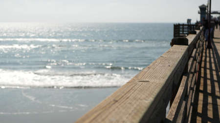 Railings of old wooden pier, people walking on waterfront boardwalk, Oceanside beach atmosphere,...