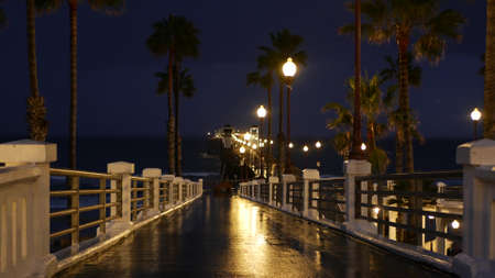 Rain drops, evening dark sky with clouds, Oceanside California USA. Empty pier and palm trees in...