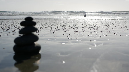 Rock balancing on ocean beach, stones stacking by sea water waves. Pyramid of pebbles on sandy shore. Stable pile or heap in soft focus with bokeh, close up. Seamless looped cinemagraph. Zen balance.の写真素材