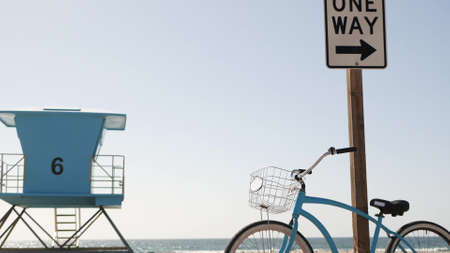 Blue bicycle, cruiser bike by ocean beach, pacific coast sky, Oceanside California USA. Summertime vacations, sea shore. Vintage cycle by road sign One Way. Lifeguard tower, rescue watchtower hut.の写真素材