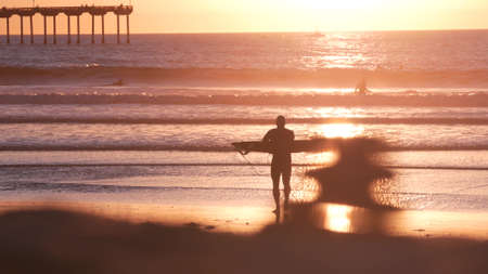 San Diego, California USA - 28 Nov 2020: People surfing by Ocean Beach pier on piles at sunset. Surfers on surfboards in water waves. Vacations on pacific coast or shore. Recreational sport hobby.のeditorial素材