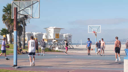 San Diego, California USA - 19 Nov 2020: Young people play basketball on beach, court for basket ball game players. Active men on coast sport field, teenagers on streetball playground, Mission beach.のeditorial素材