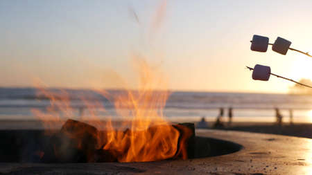 Campfire pit by Oceanside pier, California USA. Camp fire on ocean beach, bonfire flame in cement ring place for bbq, sea water waves. Heating, roast or toast marshmallow on stick. Romantic sunset skyの写真素材