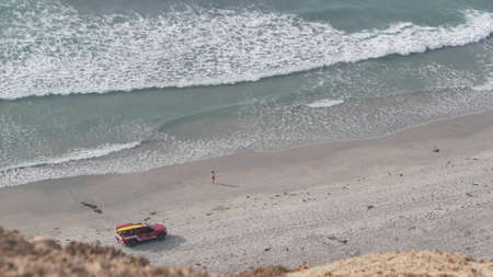 Lifeguard red pickup truck, life guard auto on sand, California ocean beach USA. Rescue pick up car on coast for surfing safety, lifesavers vehicle and sea waves tide from above. Torrey pines cliffs.の写真素材