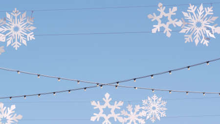 Artificial carton snowflakes, street decor for Christmas and Happy New Year. White wooden snow flakes and light bulb garland in sky, festive winter holiday decoration for Xmas celebration in december.の写真素材
