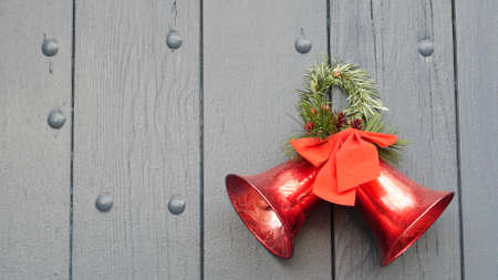 Christmas and New Year decor, pine or fir, red ribbon and bells on door or gate. Xmas vintage festive decoration from tree hanging on wooden entrance in december. American holiday tradition in USA.の写真素材