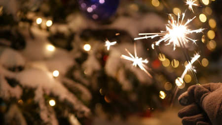 Sparkler firework burning, Christmas tree in snow, New Year or Xmas bengal light. Decorated spruce, pine or fir in snowflakes . Winter holiday fairy magic, sparkles glow, flakes and golden stars bokehの写真素材